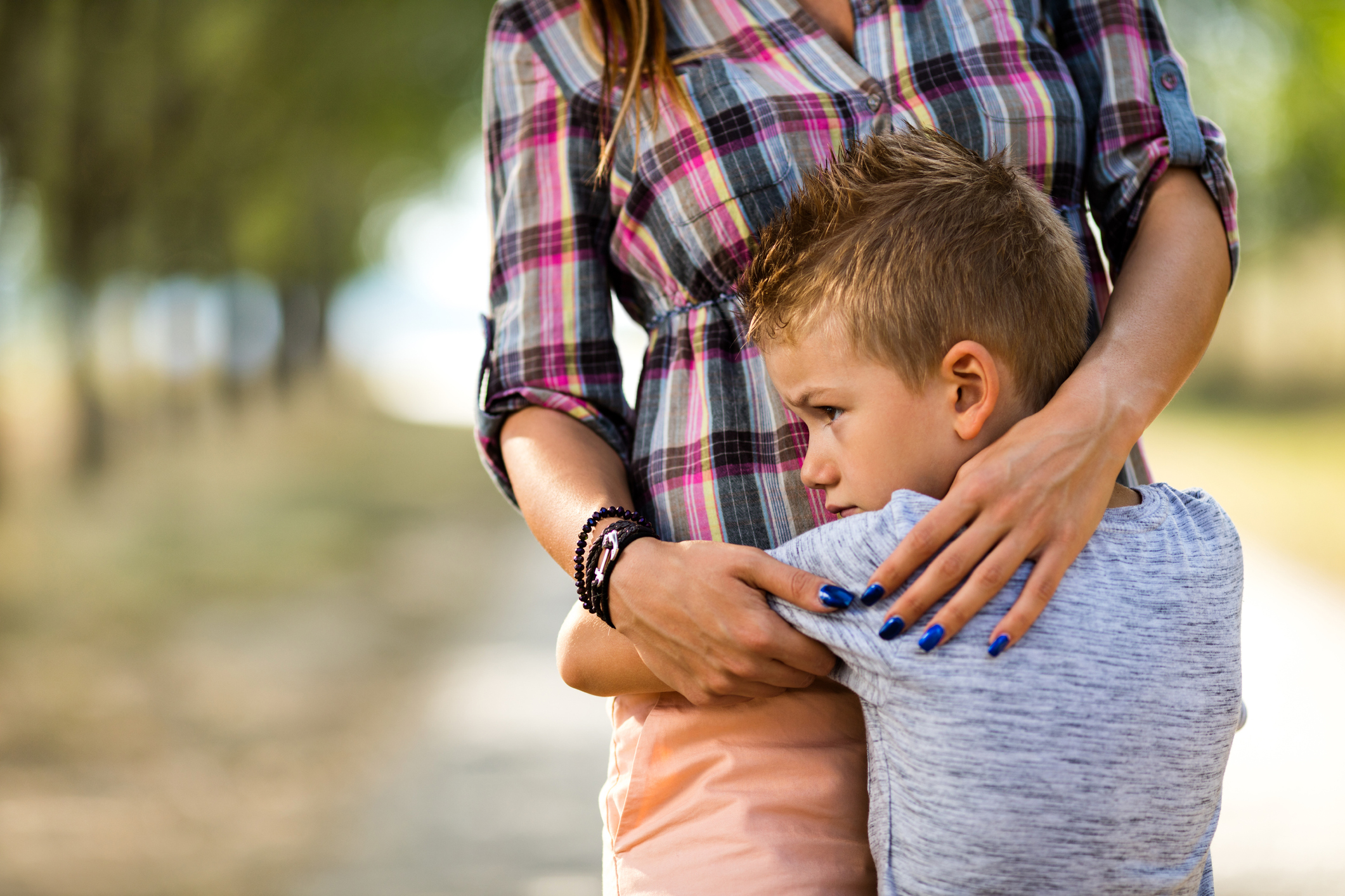 Worried little boy at the park embracing his unrecognizable mother.