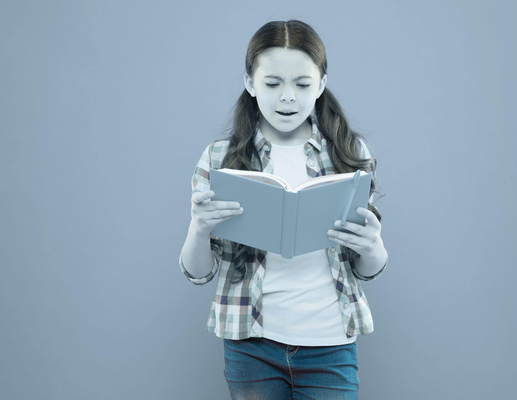 A gray tone image of an early elementary age girl holding an open book.