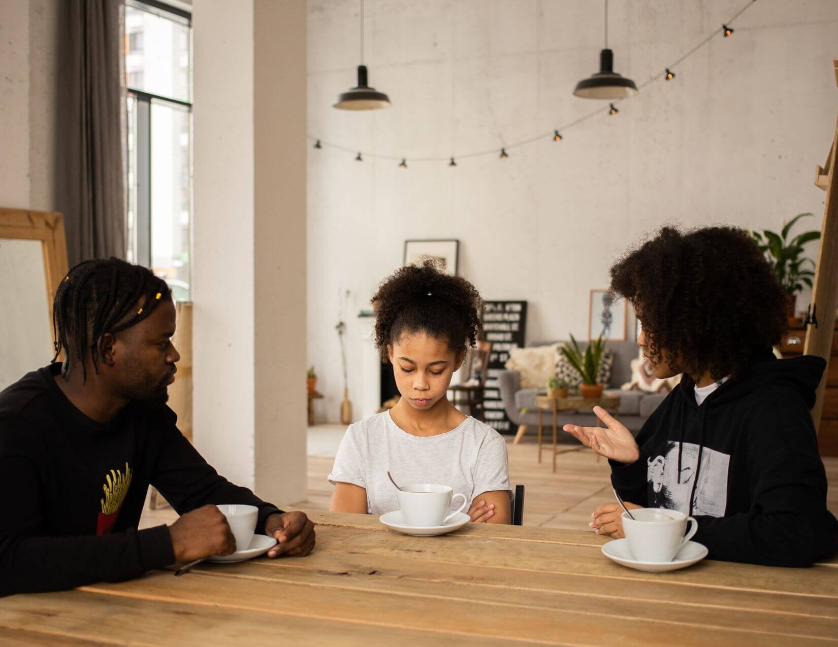 Girl sits at table with her parents. She is looking down while her parents are looking at her.