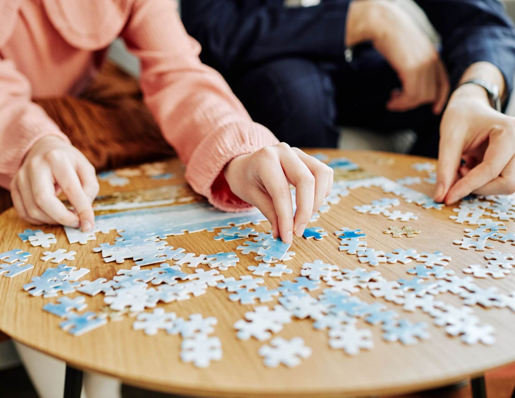 The hands of a child and an adult work on a jigsaw puzzle on a small table.