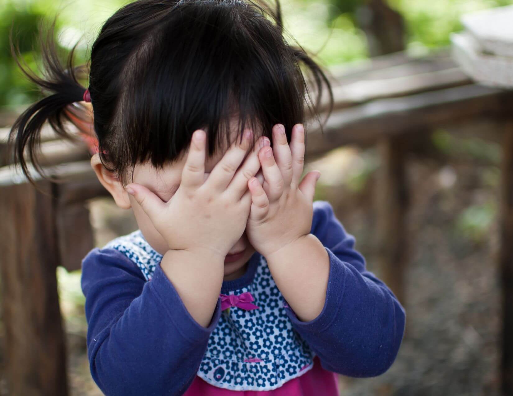 Social Presence Toddler with dark brown ponytails holding her hands over her eyes.