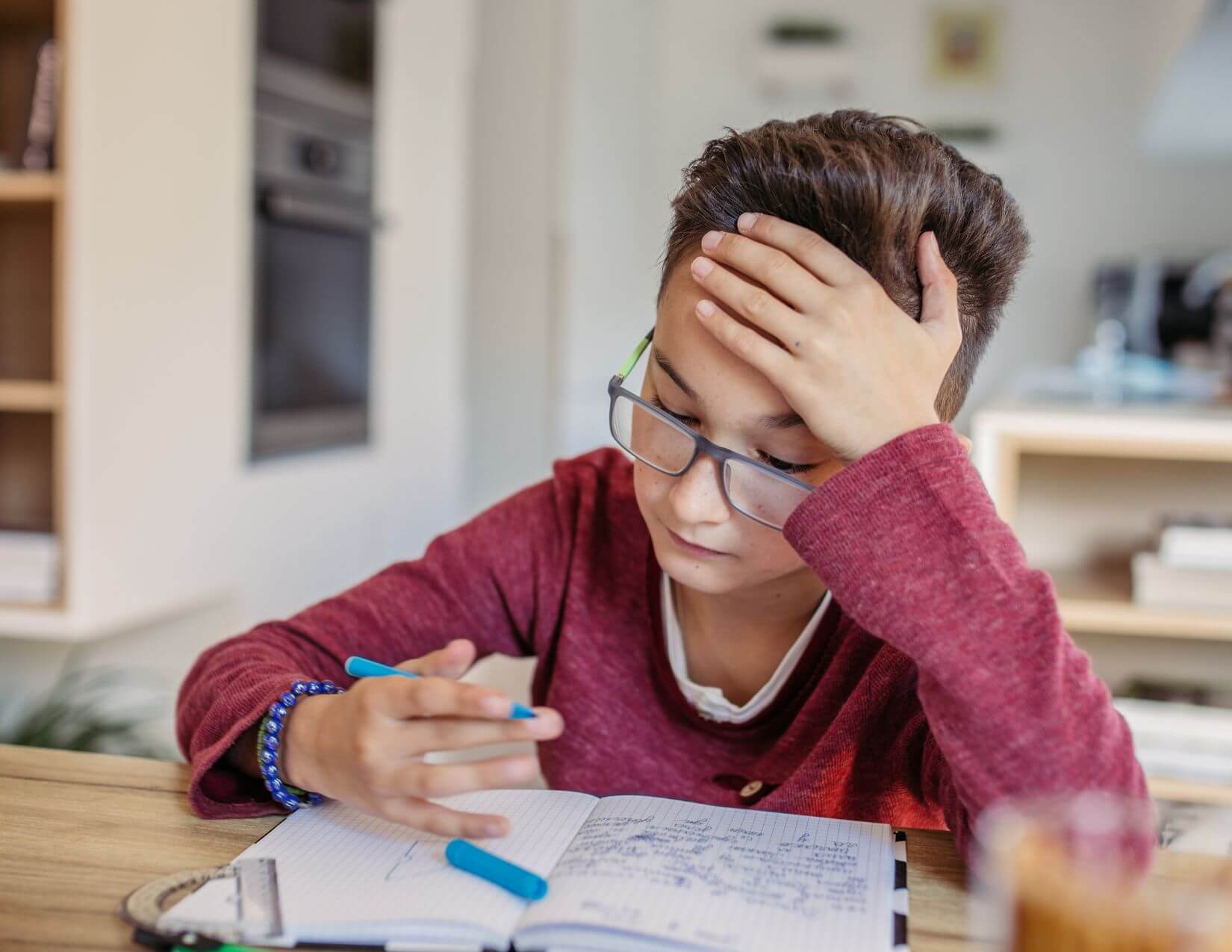 Initiation School-aged boy with light skin and brown hair sitting at a table with an open notebook of writing in front of him.